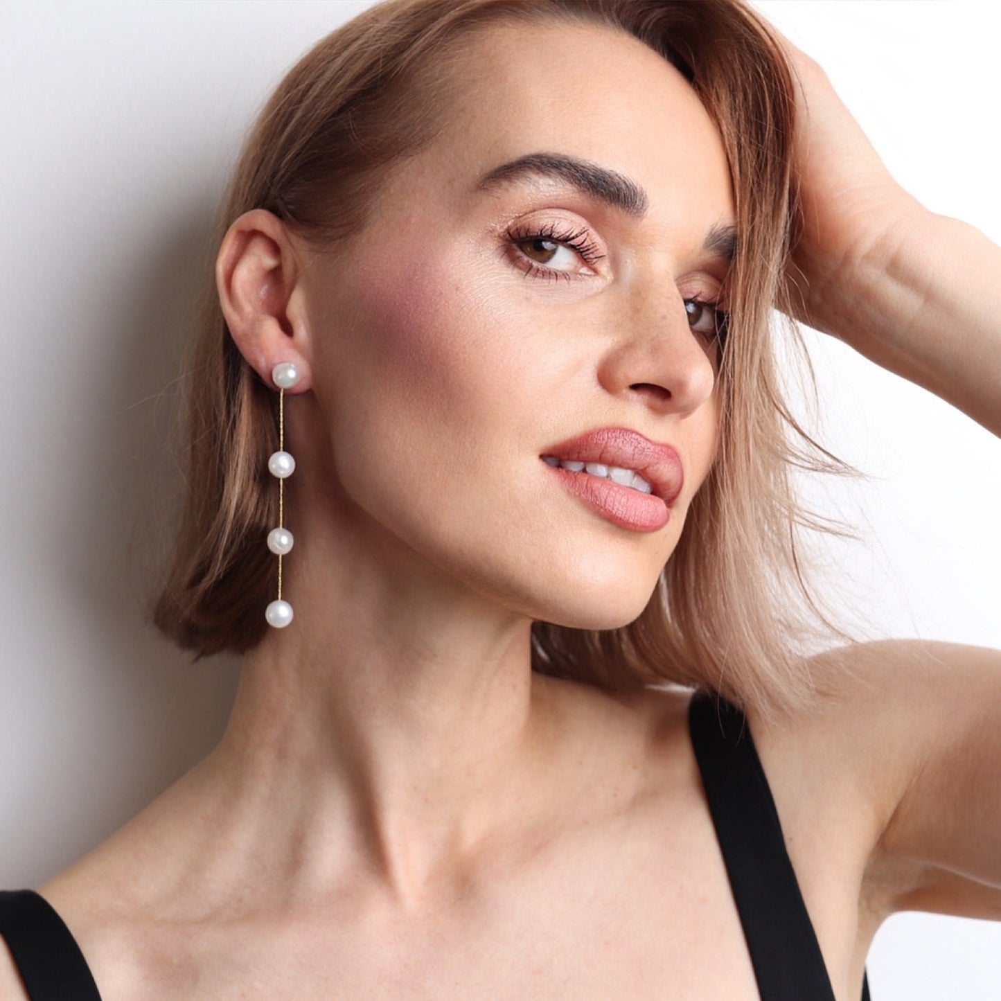 Boucles d’oreilles pendantes dorées avec perles naturelles blanches portées par une femme pour un mariage