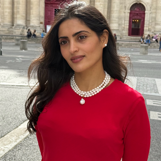 Collier de perles Lady Diana trois rangs porté avec un pull rouge dans une rue de Paris