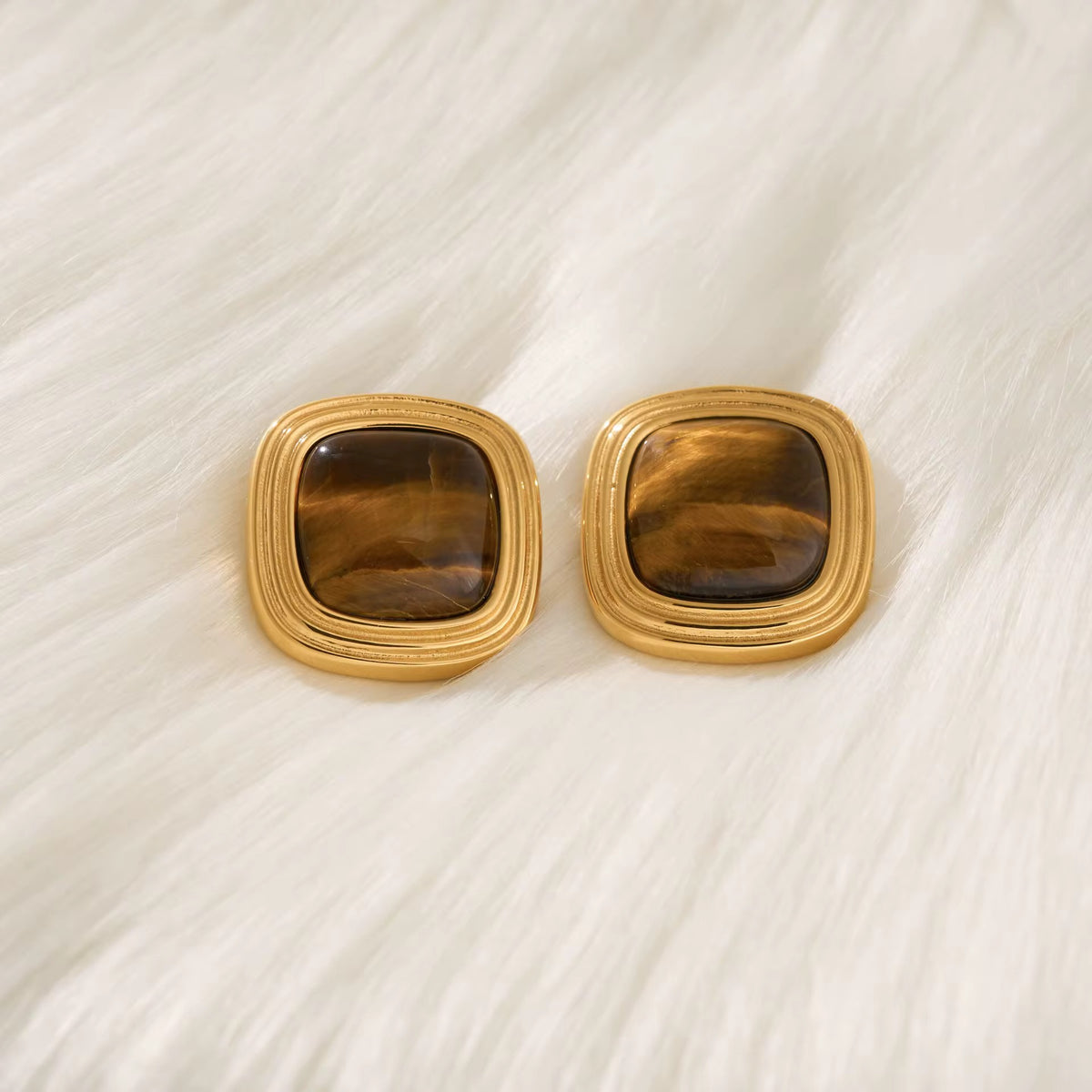 Paire de boucles d'oreilles carrées œil de tigre dorées sur une fourrure blanche