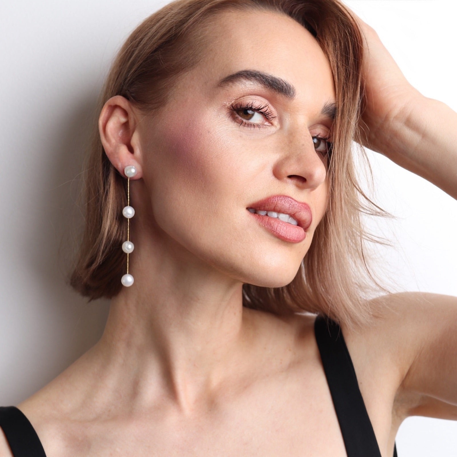Boucles d’oreilles pendantes dorées avec perles naturelles blanches portées par une femme pour un mariage