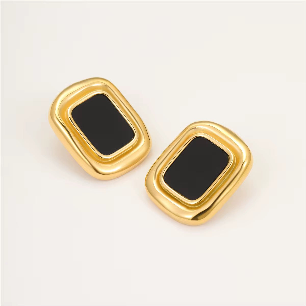 Paire de boucles d'oreilles Marylou dorées à pierre noire posées sur fond crème