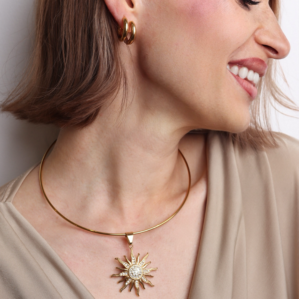 Tour de cou modulable doré porté avec pendentif soleil XL serti de pierres de zirconium.