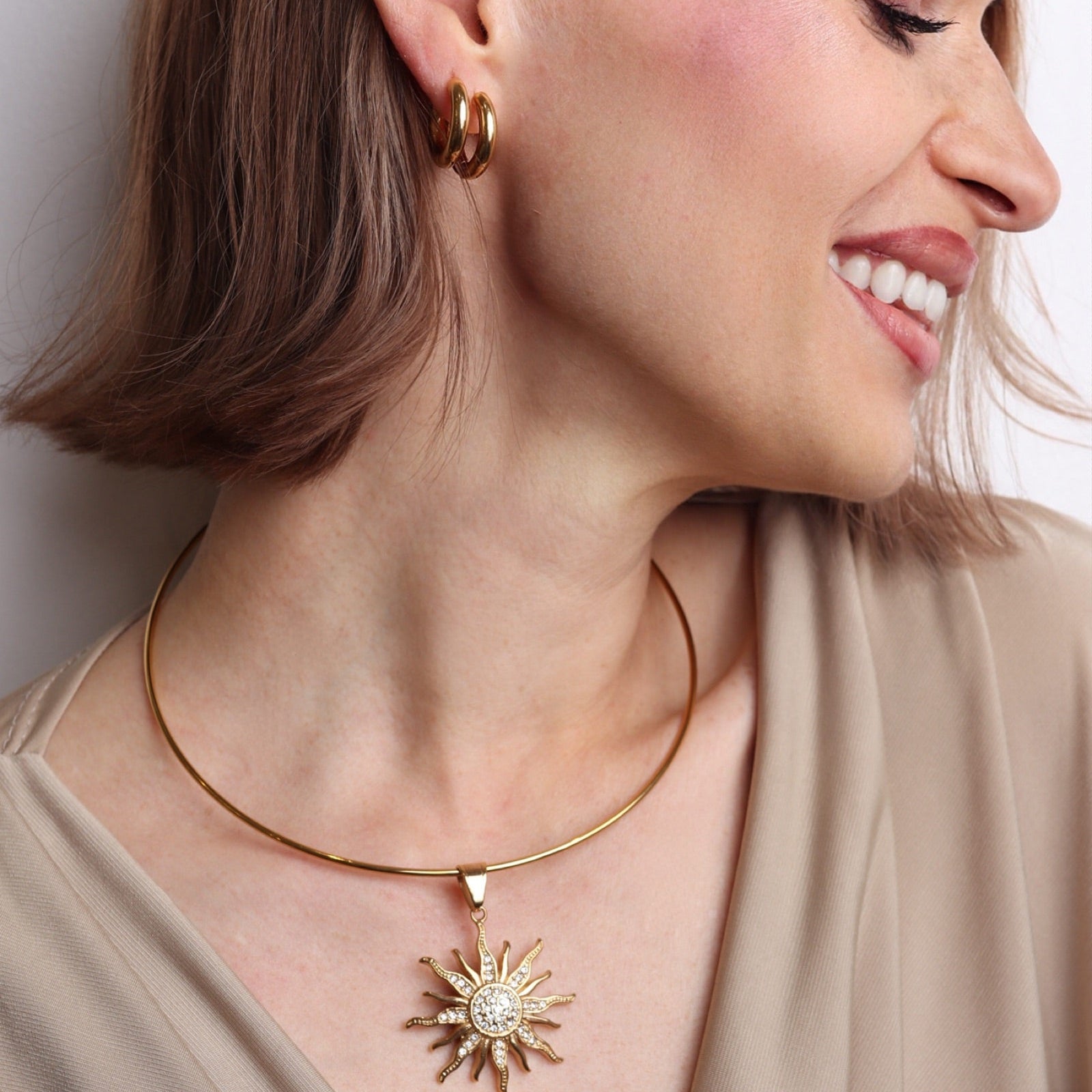Femme portant un choker doré rigide avec pendentif soleil XL serti de strass