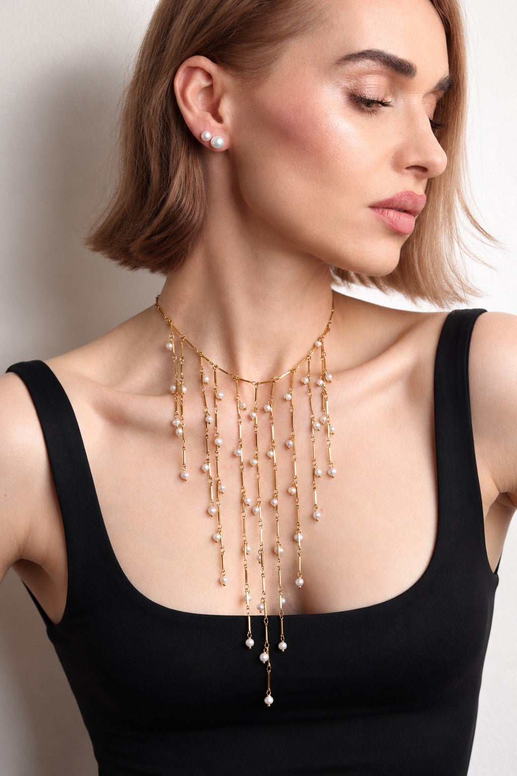 Collier plastron Séraphine doré porté sur un top noir à encolure carrée, franges de perles