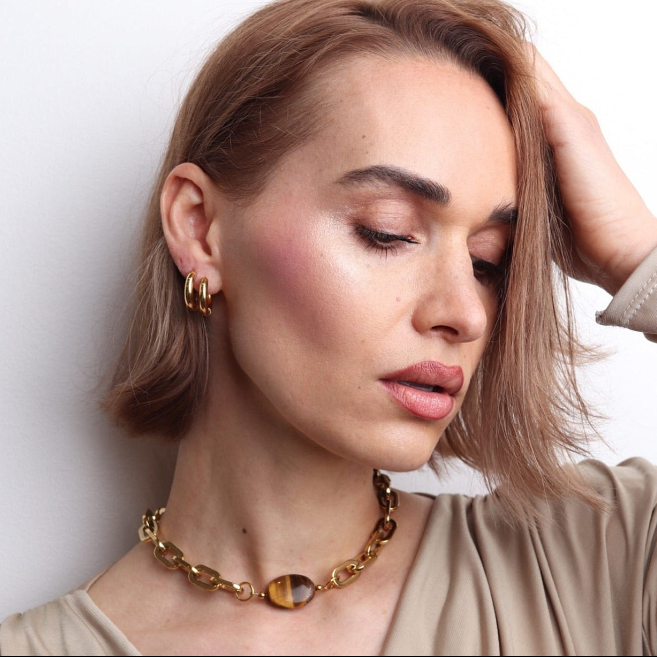 Collier interchangeable doré avec pierre œil de tigre marron au centre porté par une femme au style chic et moderne