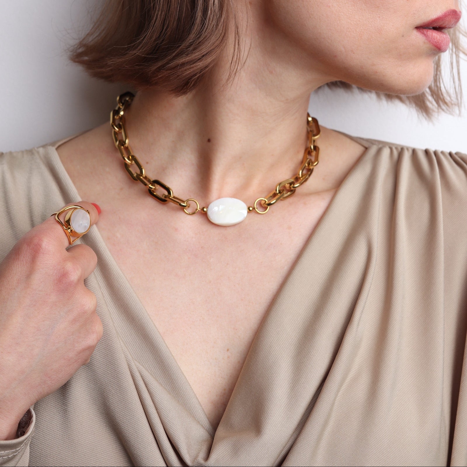 Collier doré à grosse maille collier modulable interchangeable avec pierre blanche nacrée au centre porté par une femme au style chic et moderne